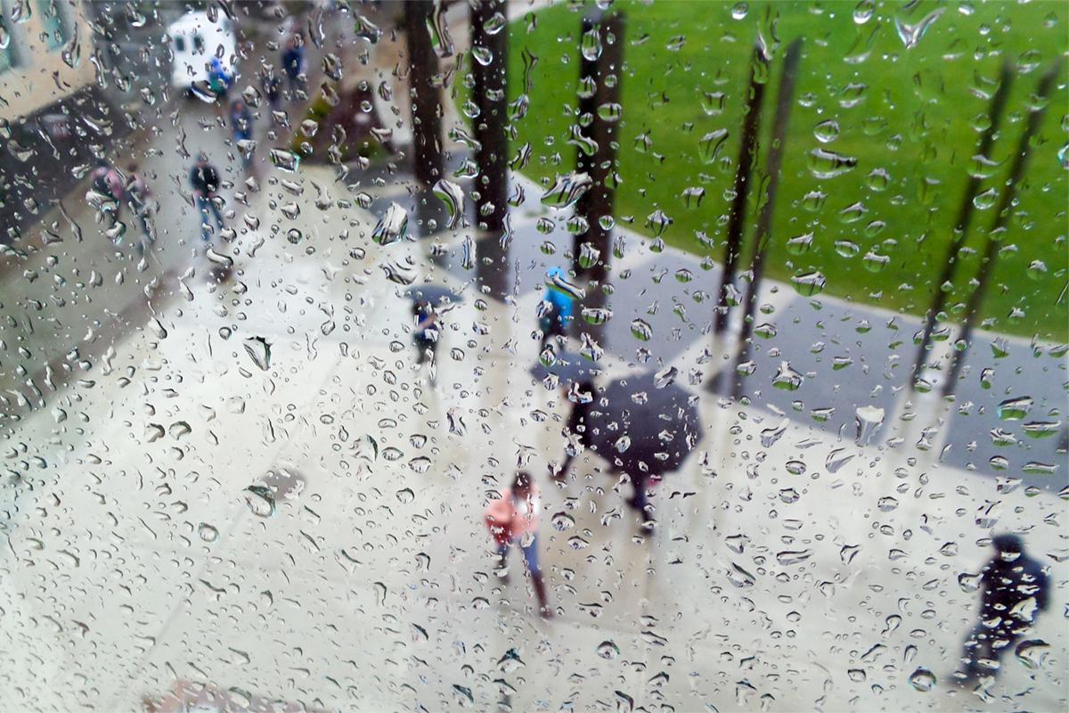 Aerial view through a rainwashed window of students walking across the Trustee Plaza, some with umbrellas